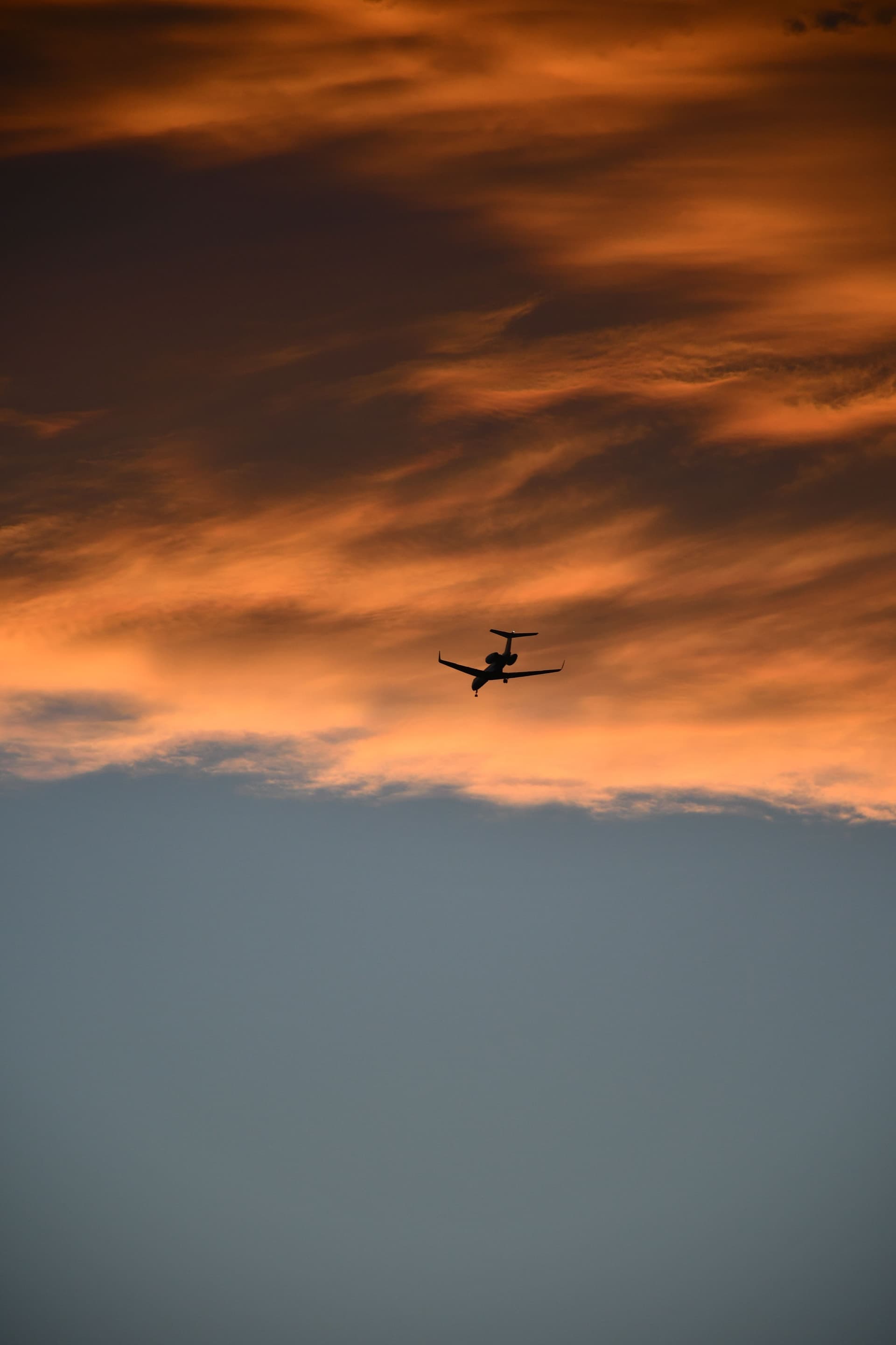 Silhouette of a jet flying beneath orange sunset clouds