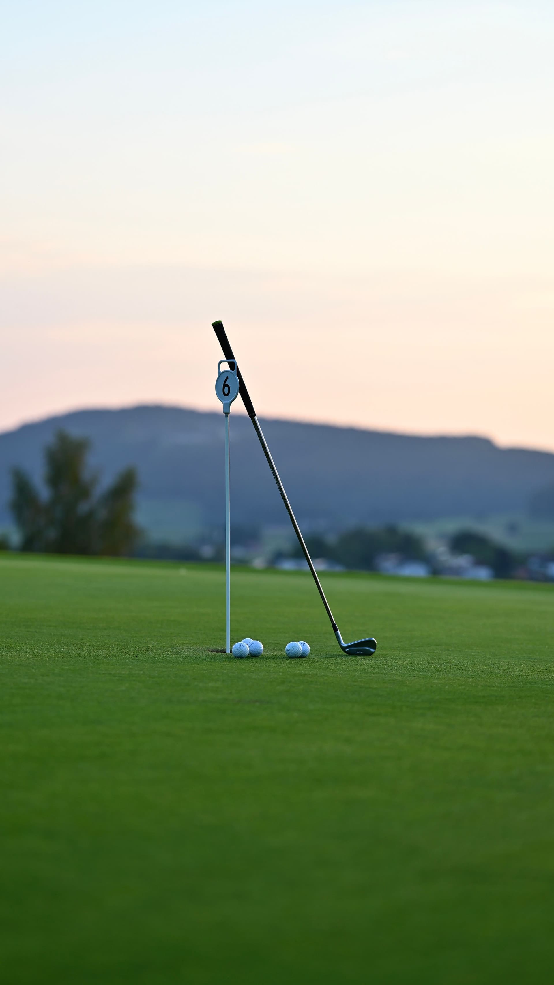 Golf club and balls beside a numbered marker on a golf green